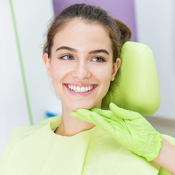 Smiling woman in green dental bib with green gloved hand on chin